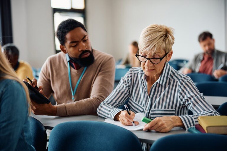 Mature woman studying with help of teacher during adult educational training class.